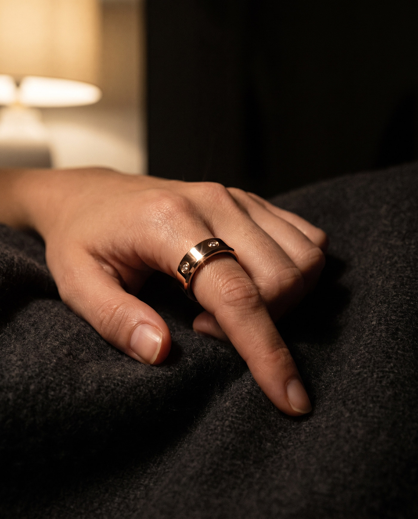 The LuxenX ring worn on the index finger, hand resting on a dark blanket by lamplight